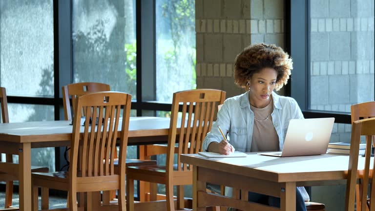 Young African-American woman using laptop, taking notes