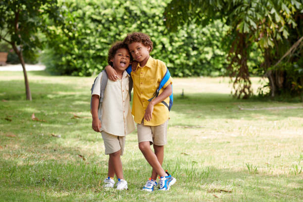 Brothers with backpacks standing on school backyard, hugging and looking at camera
