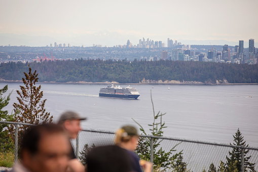 North Vancouver, Canada - August 6, 2023. A cruise ship passes by at the Cyprus Pop-up Village viewpoint in North Vancouver. People gather by the view.