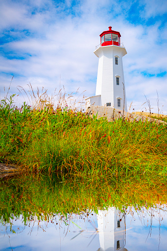 Peggy's Cove Lighthouse on the rocky hilltop and water reflections, in Nova Scotia, Canada