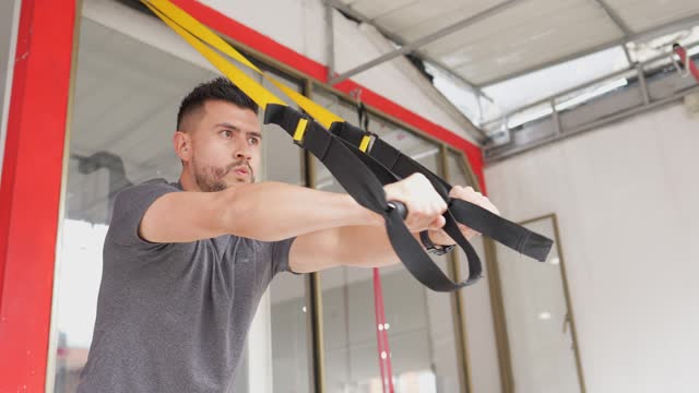 Fitness man exercising with suspension straps at the gym