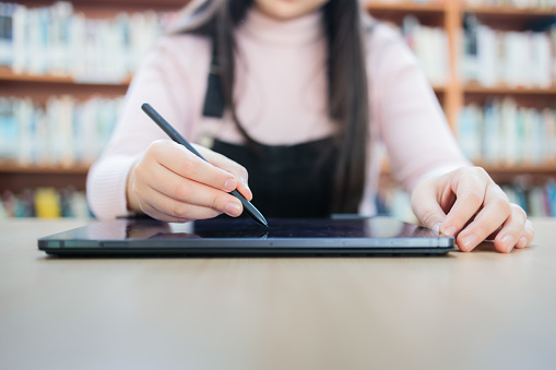 Close up of unrecognizable Female University Design Student using her Tablet and pen at the Library