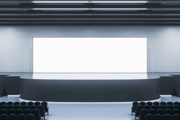 istock Clean exhibition hall interior with illuminated empty white mock up banner on stage. Auditorium and advertisement concept. 1614934614