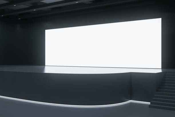 istock Modern exhibition hall interior with illuminated empty white mock up poster on stage. Auditorium and advertisement concept. 1614936198