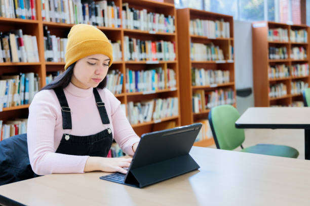 istock Academic Pursuits: Young Female University Student Studying and typing a text on her Tablet at the Library 1614936544