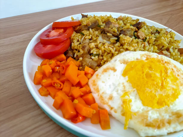 une assiette de riz frit avec de l’agneau, un œuf au plat, de la tomate et de la carotte isolée sur du bois texturé. nasi goreng kambing, cuisine indonésienne - beef rice orange stir fried photos et images de collection