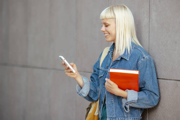 istock Young female student using smart phone in front of gray wall 1614991995