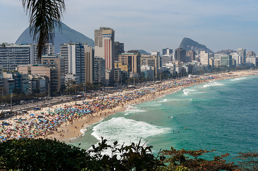 Leblon and Ipanema beach in Rio de Janeiro, Brazil. Sunny day with blue sky and many people on the beach. Plenty of umbrellas on the sand. Weekend. Turquoise and clear sea.