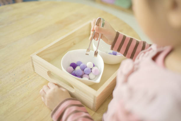 Preschool mixed girl transferring pom-pom with tong, practical life skill activity, preliminary exercises in Montessori education school