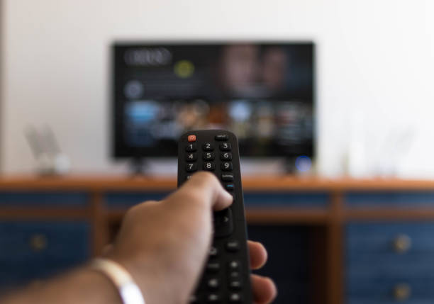 Hand holding remote control while searching for a series on television