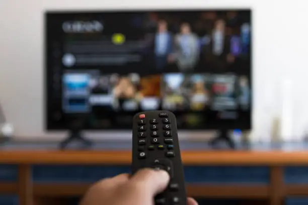 Photo of Hand holding remote control while searching for a series on television