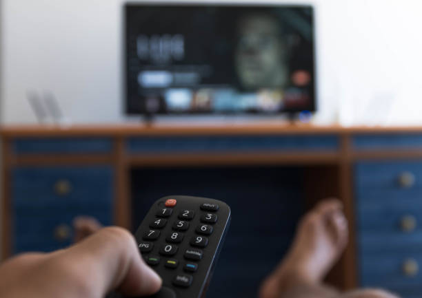 Hand holding remote control while searching for a series on television with hit feet on the table