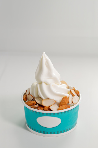 Vanilla yogurt soft ice cream with almonds topping in a cup in white background