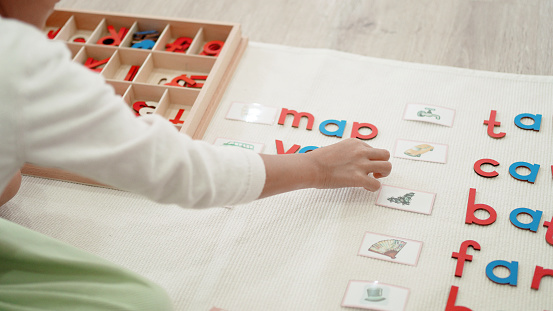 Elementary girl learning words and phonetic spelling using moveable alphabet in Montessori education school and homeschooling