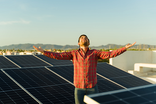 Excited young man smiling while celebrating financial liberty by saving money using solar panels and clean energy at home