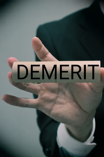 A picture of a person holding a building block that says DEMERIT
