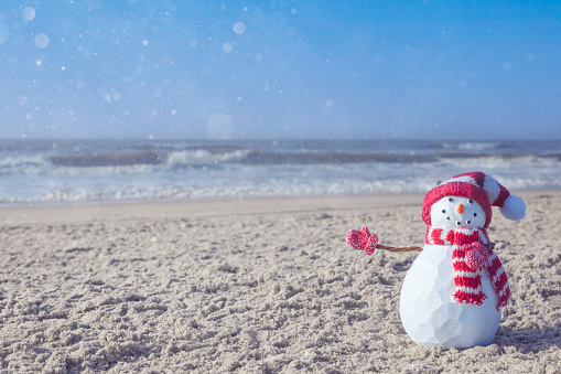 Snowman at the beach, in the sand by the ocean. For winter holidays, Christmas and New Years.