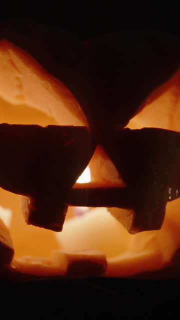 Vertical video. A Halloween pumpkin with candles burning inside. The camera's focus slowly zooms in on it.