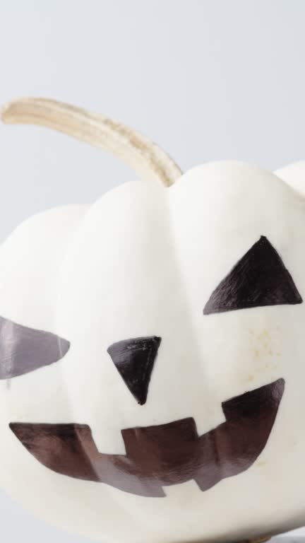 Vertical video. A painted white Halloween pumpkin spins on a white background. Close-up view.