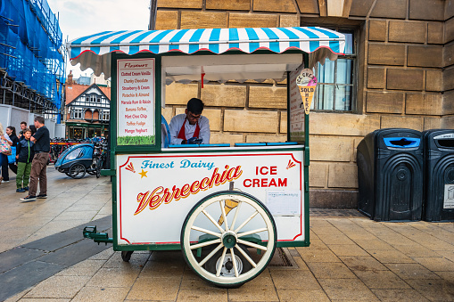 Vendor stands at ice cream cart in downtown Cambridge, Cambridgeshire, England, UK on an overcast day.