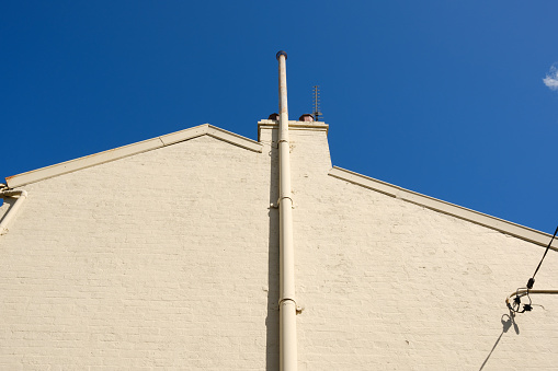 Close-up on a side wall of a building with chimney and deep blue sky beyond.