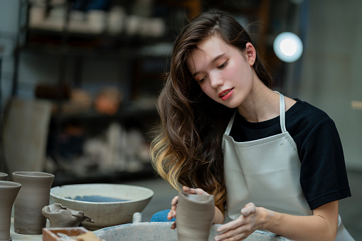 Engaged in pottery alchemy, a young woman transforms clay through precise scraping, molding her creation with skill.