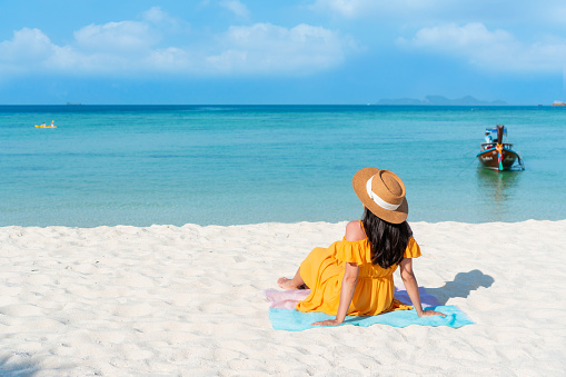 Happy traveler Asian woman on yellow dress relax on the tropical sandy beach. Summer, holiday concept. Free space