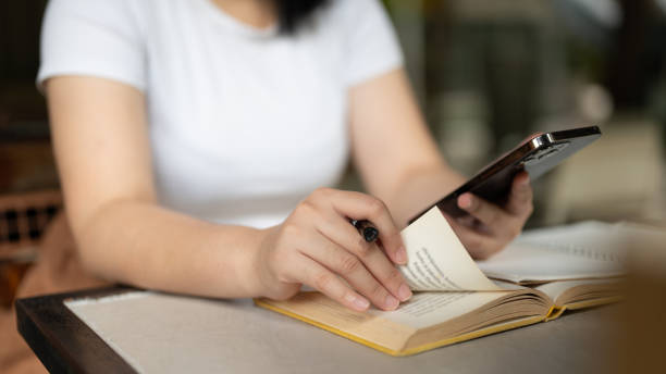istock Close-up image of a female freelancer using her smartphone while reading a book in a coffee shop. 1615625901