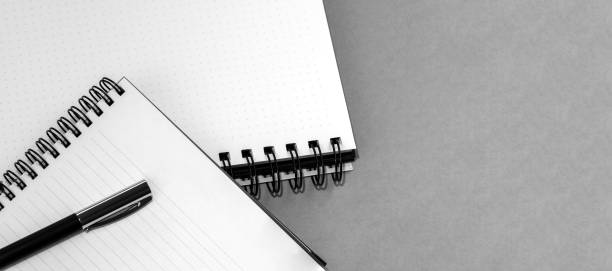 Notebook with a spiral and pen on a blank sheet. Neutral gray textured background. View from above