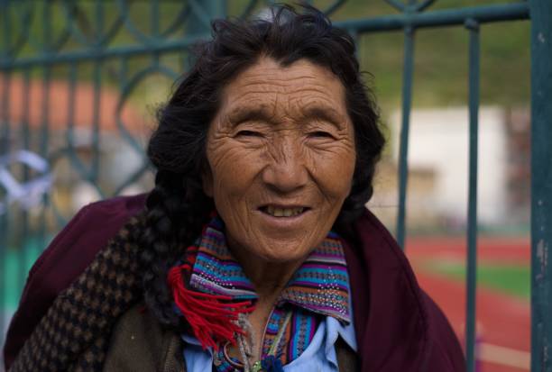 Bumthang Valley, Bhutan - April 17, 2008: A Bhutanese woman dressed in a kira and silver jewelry stands near textiles woven from yak hair on a mountain pass in the Himalayans, Asia