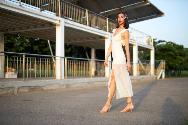 A graceful woman adorned in a radiant blue strapless evening gown, featuring elegant ruching and a dramatic thigh-high slit, subtly adjusting the flowing fabric. Her poised stance and the shimmering details of the dress, complemented by stylish high heels, create a vision of sophistication and allure. This image is perfect for themes of fashion, special occasions, and timeless elegance.
