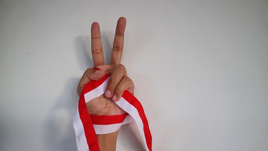 hands gesturing hold in fist, independence symbol wearing Indonesian red and white ribbon. Indonesia's independence day concept.