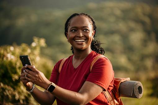 With her hiking gear and backpack, a black woman confidently climbs the hills, glancing at her phone to ensure she stays on the right path indicated on the map.