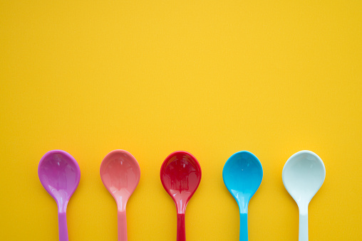 Flat lay of colorful spoons on yellow background copy space. Food, kitchen utensil, creative design concept.