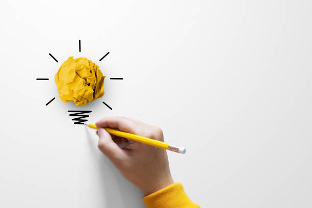 istock Creative thinking ideas and innovation concept. Paper scrap ball yellow colour with light bulb symbol on white background and hand holding yellow pencil 1615754297