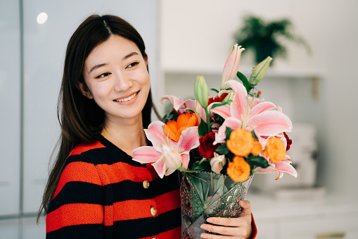 Portrait of beautiful woman holding a fresh flower bouquet and enjoying at home.