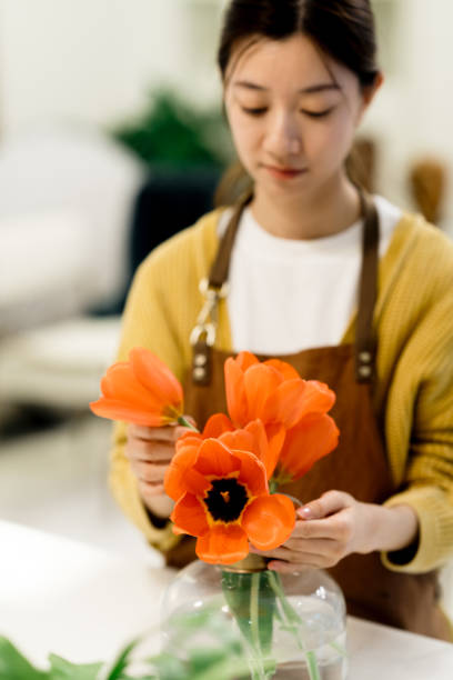 joven asiática arreglando un ramo de flores en un jarrón de vidrio en casa. - scented asia asian culture bunch fotografías e imágenes de stock