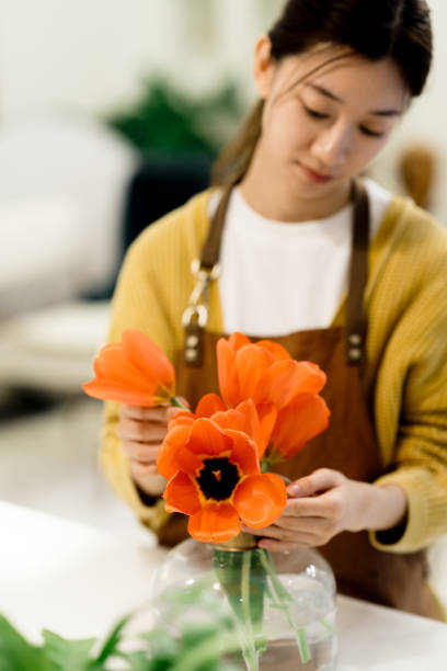 joven asiática arreglando un ramo de flores en un jarrón de vidrio en casa. - scented asia asian culture bunch fotografías e imágenes de stock