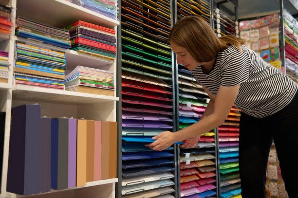 istock Caucasian female sales manager arranges multi colored cardboard paper sheets on retail shelves in a creative art store 1615848203