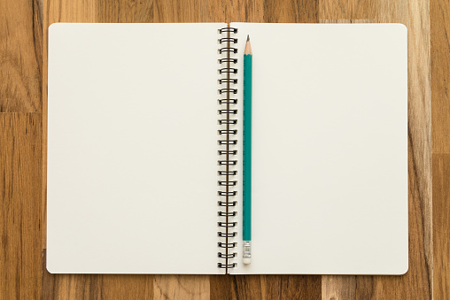 Flat lay of open blank spiral notepad or notebook and pencil on wooden table background. Office supply stationary, diary, organizer, business, education concept.