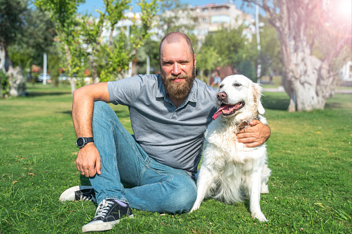 Portrait of Man pet owner with his happy pet dog golden retriever outside on lawn public park during summer.