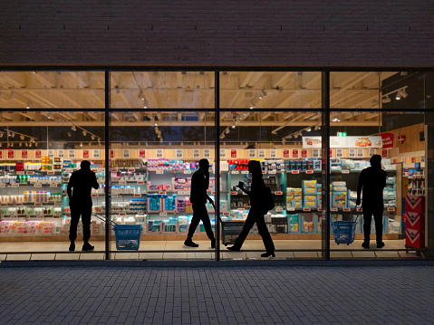 A look through a window in a supermarket at night. People go shopping.