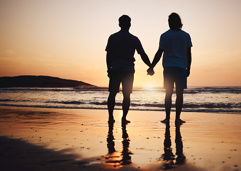 Silhouette, holding hands and gay couple on beach, sunset and nature on summer vacation together in Thailand. Sunshine, ocean and romance, lgbt men on island and fun holiday with pride, sea and waves
