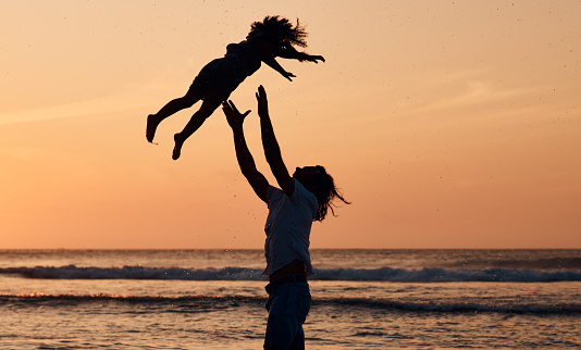 Child, sunset or father by ocean to play a game in Rio de Janeiro in Brazil with support, care or love. Throw, parent and lifting kid in air at sea to enjoy family bonding together in nature by water