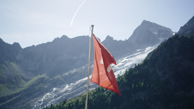 Swiss flag waving in the wind, glacier and alps behind