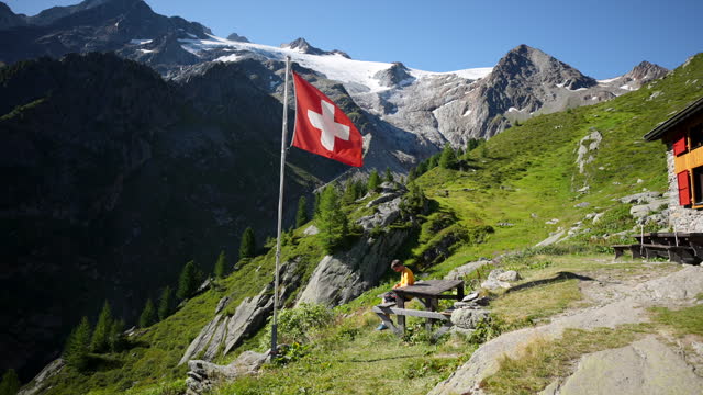 Trail runner rests at mountain hut, view of swiss flag and glacier in the background