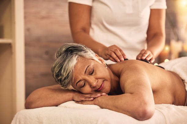 massage de la femme, du spa et de la pierre pour la guérison des muscles du dos, traitement de la peau et thérapie holistique au salon de beauté. une femme mature se détend dans un centre de bien-être avec des roches pour prendre soin de soi, se dési - massaging spa treatment stone massage therapist photos et images de collection