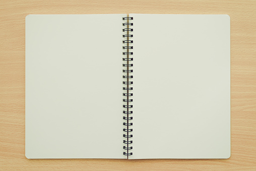 Blank empty spiral notebook on wood table background copy space. Business, education, stationary concept.