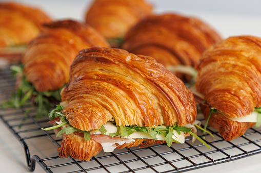 Close-up on  baked croissants, filled with prosciutto, cheese and arugula leaves on a serving grid
