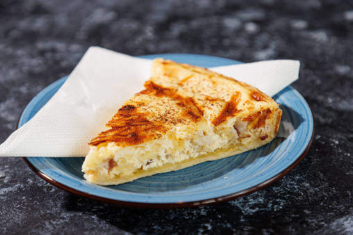 Baked slice of cheese pie with yellowish brown crust on top, served on a plate in cafeteria